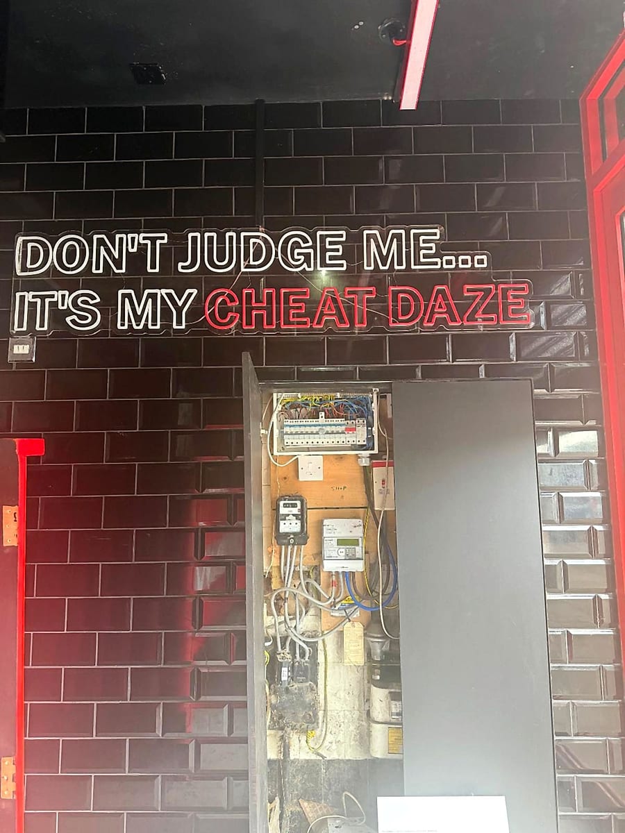 The new consumer unit at Cheat Daze in its cupboard beneath the Don't Judge Me, It's My Cheat Daze neon sign