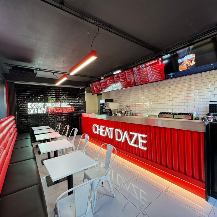 A finished Cheat Daze dessert bar: suspended linear lights, the illuminated red counter, neon wall sign and menu screens