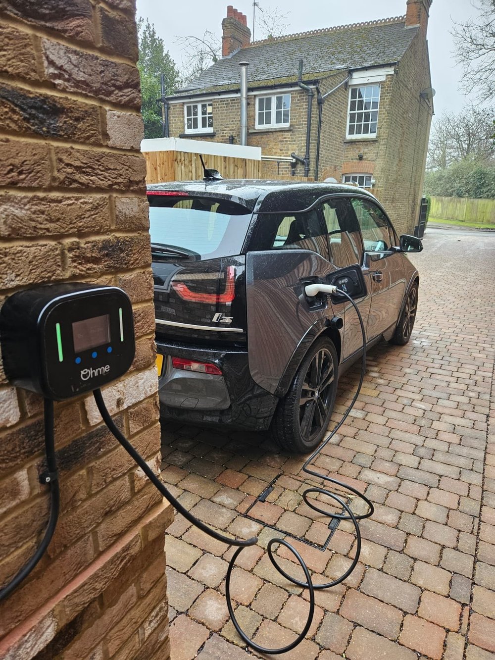 Home EV charger fitted to a red brick wall, car charging on the driveway